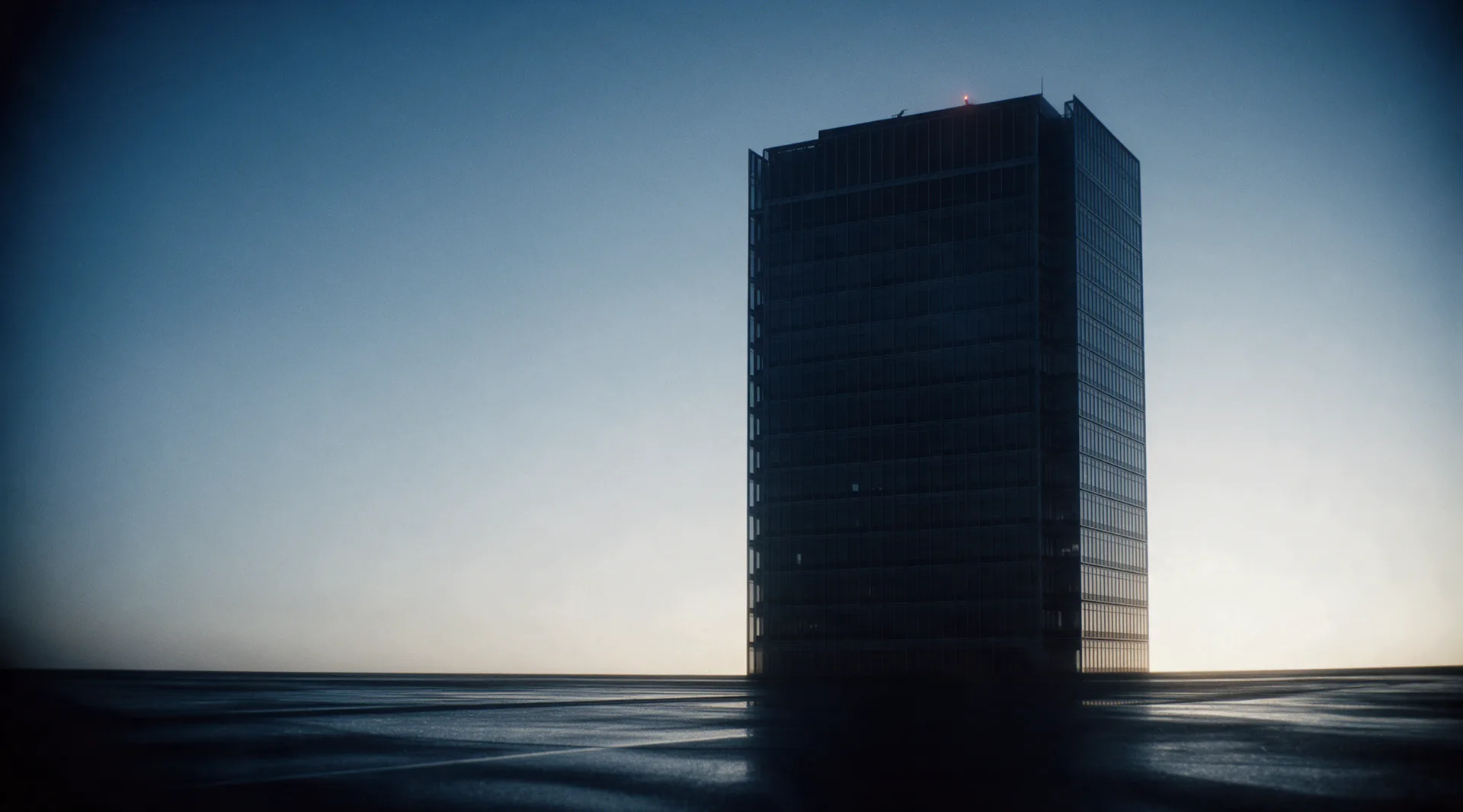 The same office tower at first light, every window dark and the street drying